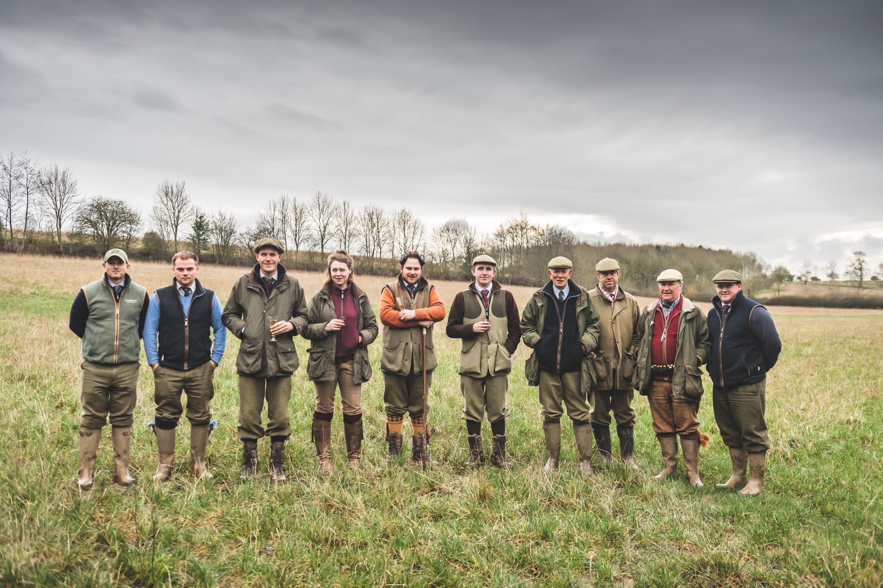 group of people standing in green grass field wearing tweed and wellies